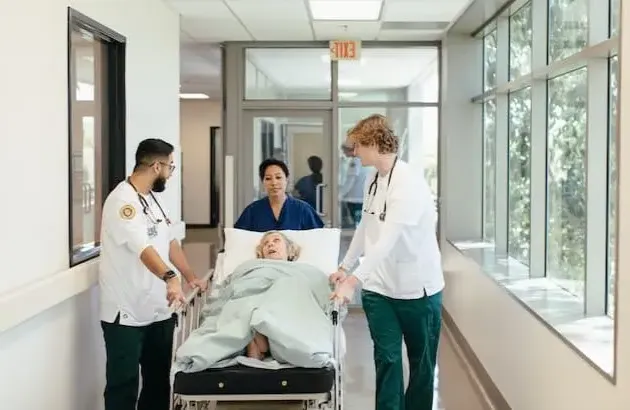 护理 students moving patient in hospital bed down the hall